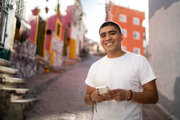 porträt eines jungen mannes mit smartphone auf der straße - lateinamerikaner oder hispanic stock-fotos und bilder