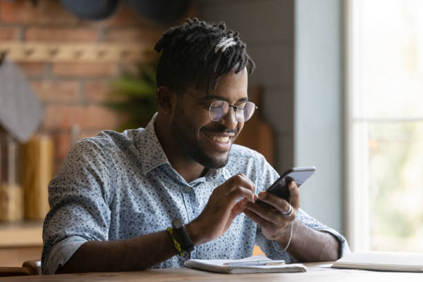 istock Happy young african american man sit at table use phone 1311634214