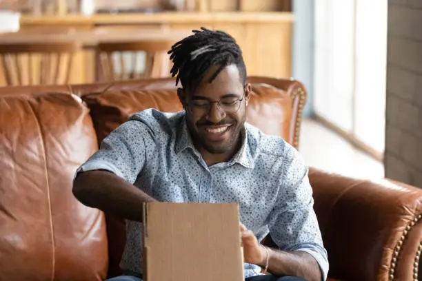 Photo of Excited black male web shop customer unpack small cardboard box