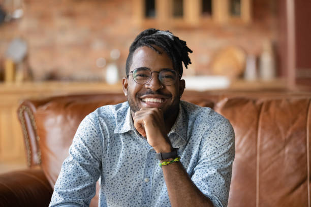 istock Smiling young black male sitting on sofa looking at camera 1311634253