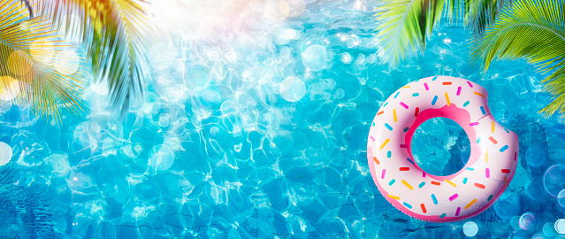 Donut inflable en piscina con hojas de palma y luz solar photo