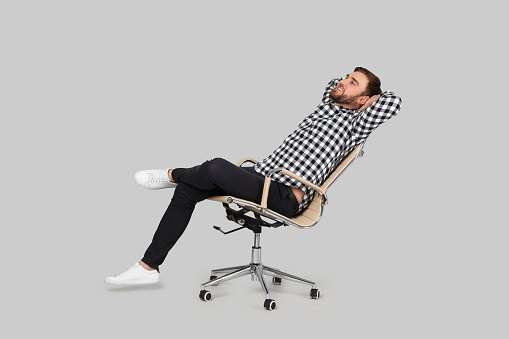 Young man relaxing in comfortable office chair on grey background