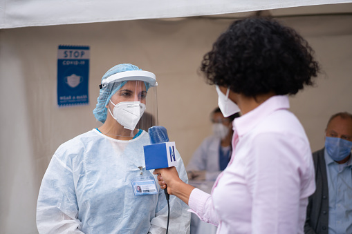 Journalist interviewing a healthcare worker working at a COVID-19 vaccination stand during the immunization program - news concepts
