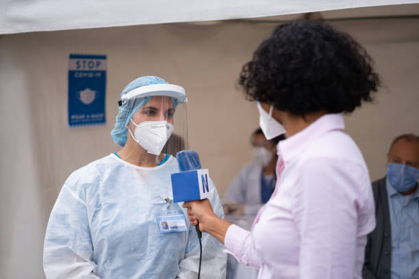 Journalist interviewing a healthcare worker working at a COVID-19 vaccination stand Journalist interviewing a healthcare worker working at a COVID-19 vaccination stand during the immunization program - news concepts tv reporter photos stock pictures, royalty-free photos & images
