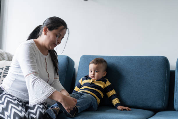 Mom ties her son's shoes while they are sitting on her sofa at home during Quarantine