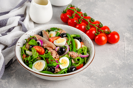 French salad Nicoise with tuna, egg, green beans, tomatoes, olives, lettuce, onions and anchovies on a gray concrete background. Healthy food
