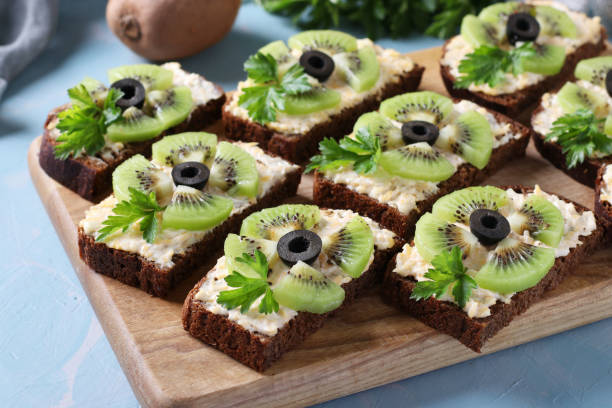 hausgemachte sandwiches mit kiwi, käse, knoblauch und schwarzen oliven auf holzbrett auf hellblauem hintergrund. closeup - foodie stock-fotos und bilder