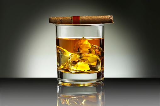 Glass of whiskey with ice cubes and cigar in crystal ashtray on white background, close-up. Alcohol drink concept, copy space provided. The scene is situated in front white background in controlled studio environment . The photo is taken with Sony A7III camera.
