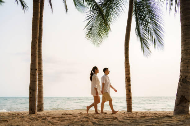 istock Asian couple is walking and holding hands on a beachfront beach sea with coconut trees while on vacation in the summer in Thailand. 1311642497