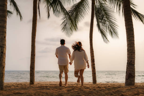 istock Asian couple is running and holding hands on a beachfront beach sea with coconut trees while on vacation in the summer in Thailand. 1311642504