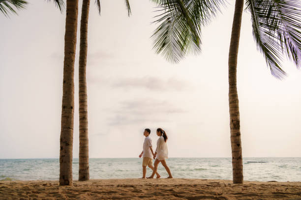 istock Asian couple is walking and holding hands on a beachfront beach sea with coconut trees while on vacation in the summer in Thailand. 1311642508
