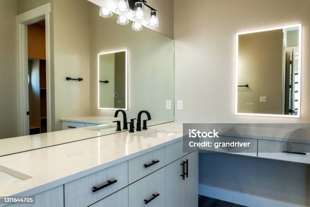 Contemporary Style Well Lit Bathroom With Sinks Cabinets And Lighted Vanity Mirror Stock Photo - Download Image Now