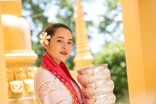 Young woman with traditional burmese holding bowl of rice on the hand at beautiful golden pagoda in Myanmar.