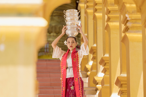 Young girl with traditional burmese holding bowl of rice on the hand at beautiful golden pagoda in Myanmar.