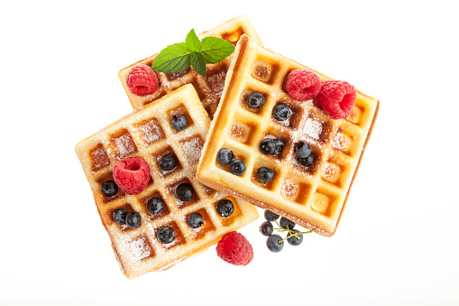 Blgian waffles with powdered sugar, raspberries and blueberries isolated on white background, high angle view