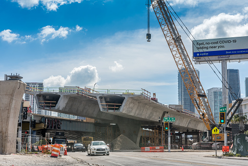 Miami, FL, USA - April 8, 2021: Heavy machinery and workers working on the construction of a new viaduct along the north of downtown Miami, where new luxury housing complexes are being developed.