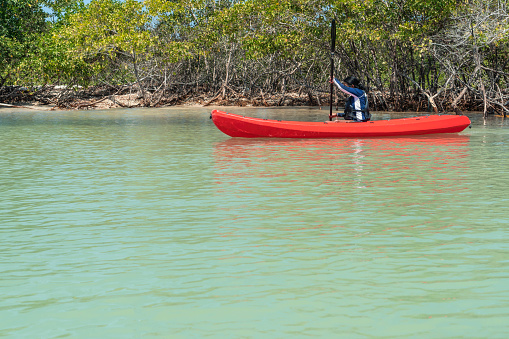 Woman enjoying a kayak ride while passing a beautiful tropical island.