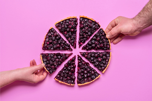 Hands grabbing slices of blueberries pie, above view minimalist. Homemade pie isolated on a purple colored background.