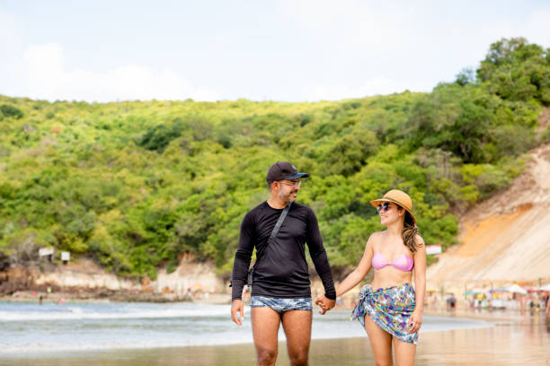 istock Smiling couple holding hands while walking together at the beach 1311668583