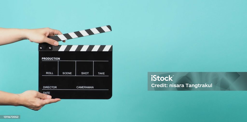 Hand is holding Black clapper board or movie slate on green or mint or Tiffany Blue background. Film Slate Stock Photo