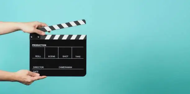 Hand is holding Black clapper board or movie slate on green or mint or Tiffany Blue background.