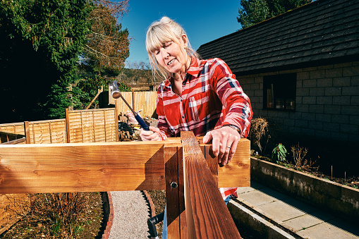 Woman erecting a wooden pergola in her back yard.