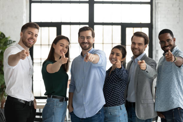 friendly multiethnic teammates pointing fingers at camera choosing new colleague - business looking at camera office new imagens e fotografias de stock