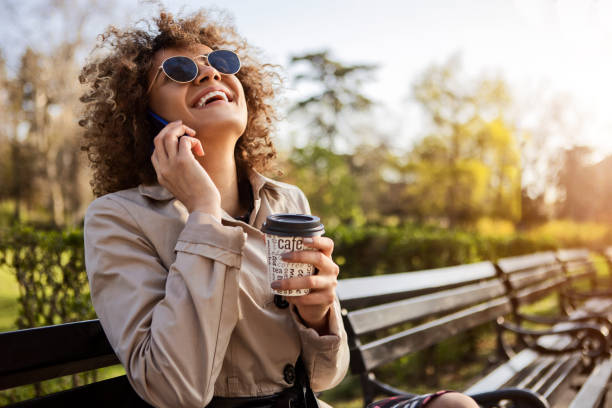 junge frau lächelnd und trinken eine tasse kaffee zum mitnehmen sprechen auf dem smartphone - telephone nature mobile phone autumn stock-fotos und bilder