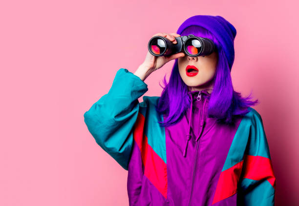 Stylish white girl with purple hair and 80s tracksuit using binoculars stock photo