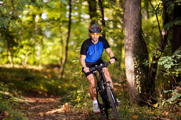Mature man on a bikepacking adventure with electric bike in nature. He is looking for camping place in pine forest. Sustainable lifestyle.