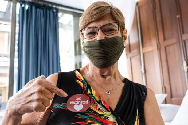 Photo of Portrait of a senior woman showing 'got vaccinated' sticker at home