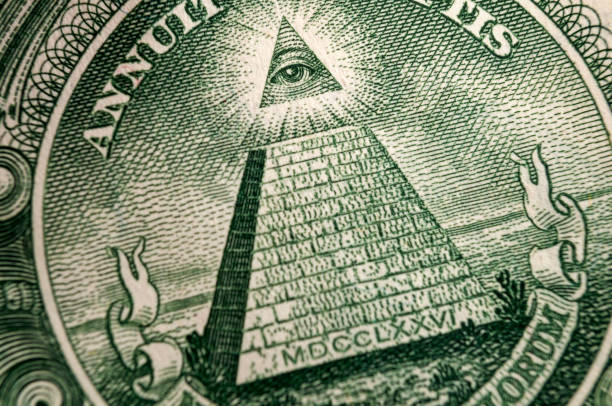 American money, illuminati and mystical symbols concept with macro close up on the all seeing eyeball atop the pyramid on the back of US dollar bill American money, illuminati and mystical symbols concept with macro close up on the all seeing eyeball atop the pyramid on the back of US dollar bill masonic symbol stock pictures, royalty-free photos & images