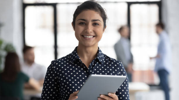 istock Smiling indian female manager standing in office holding digital tablet 1311682048