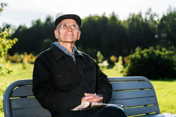 Adult man wearing eyeglasses looks up seated on bench in city park outside