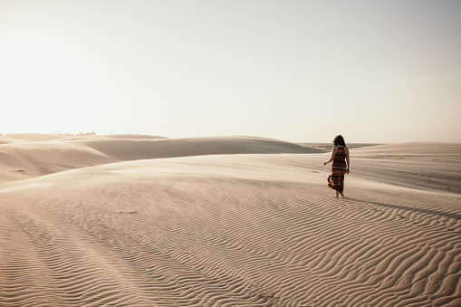Low angle view beautiful woman in long dress barefoot follow walk on KAshan desert dunes