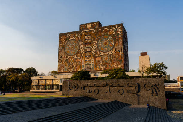 Mexico City, Mexico - January 16, 2021: Beautiful prehispanic mural on library building from UNAM under blue sky. Majestic building and yard in Mexican college. Universities and education
