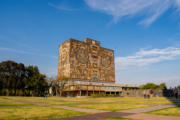 Mexico City, Mexico - January 16, 2021: Beautiful prehispanic mural on library building from UNAM under blue sky. Majestic building and yard in Mexican college. Universities and education