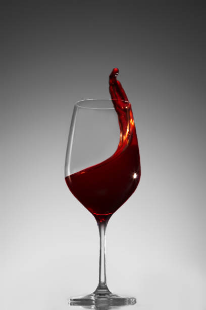 Elegant glass with red wine and a splash of wine from it on a gray gradient background. Stop motion fluid splash