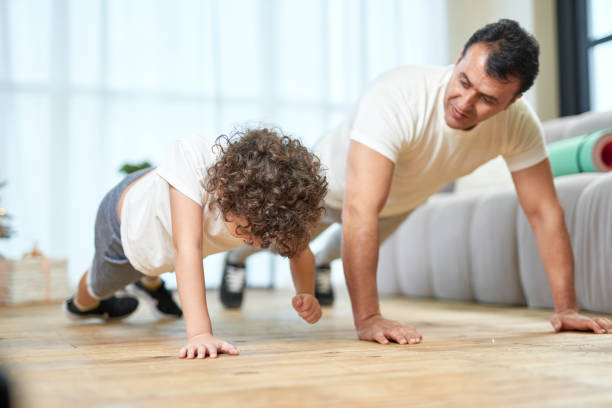 istock Training at Home. Sportive latin middle aged father teaching his son doing push ups while spending time together at home 1311697404