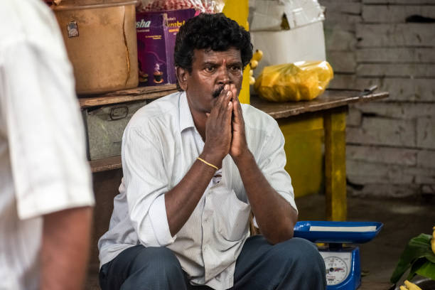 Mysuru, Karnataka, India - January 2019: An Indian street vendor sitting with his hands folded in worry and thought in an old market in the city.