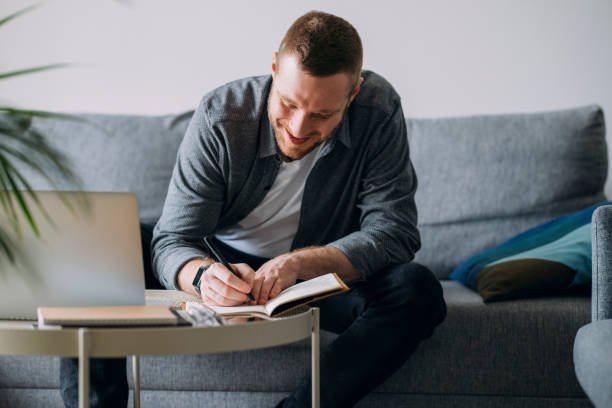 istock Work From Home: Man With Laptop Sitting On Sofa and Writing Notes 1311706527