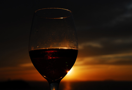 Close Up of a stemmed wine glass filled with red wine against a beautiful sunset over the sea on Naxos, Greece.