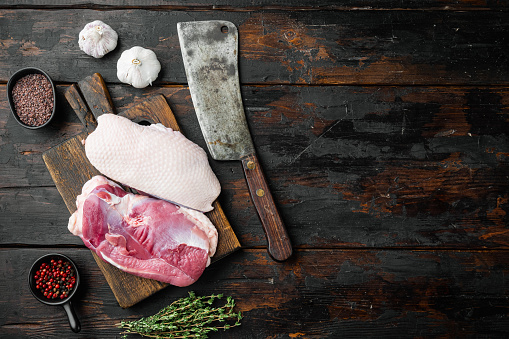 Raw uncooked poultry meat cut. Duck breast set, with herbs and ingredients, on wooden cutting board  with old butcher cleaver knife, on old dark  wooden table background, top view flat lay, with copyspace  and space for text