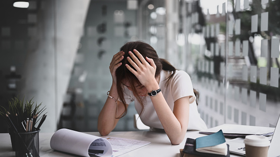 Businesswoman sitting in her workplace and holding head with hands feeling desperate or suffers from headache.