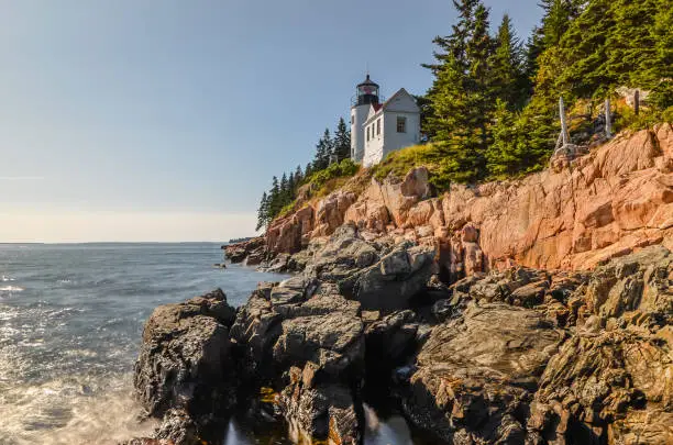 View from the rugged cliff rocks to Bass Harbor Head Light. The lighthouse was built in 1858 and is located on the coast of the US state of Maine within Acadia National Park in Mount Desert Island.