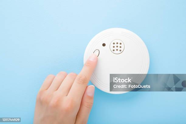Young Adult Woman Finger Pushing Button Of New White Plastic Smoke Alarm Light Blue Table Background Pastel Color Closeup Safety Concept Stock Photo - Download Image Now