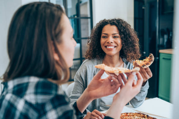 deux jeunes femmes mangeant la pizza ensemble à la maison. - soirée entre filles temps libre photos et images de collection