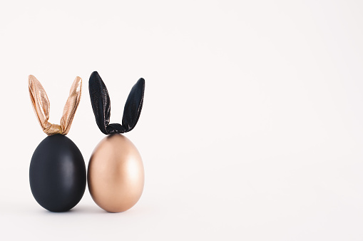 Two Easter eggs with bunny ears on a white background with copy space. Black and gold decorated eggs - rabbits.