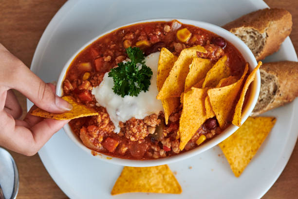 istock Young woman eats at the table chili con carne with taco chips 1311762061