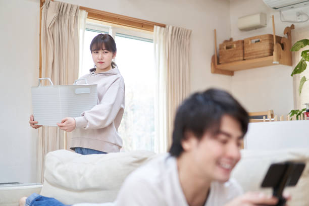 家事をしている妻とゲームをしているアジアの夫 - relationship difficulties ストックフォトと画像